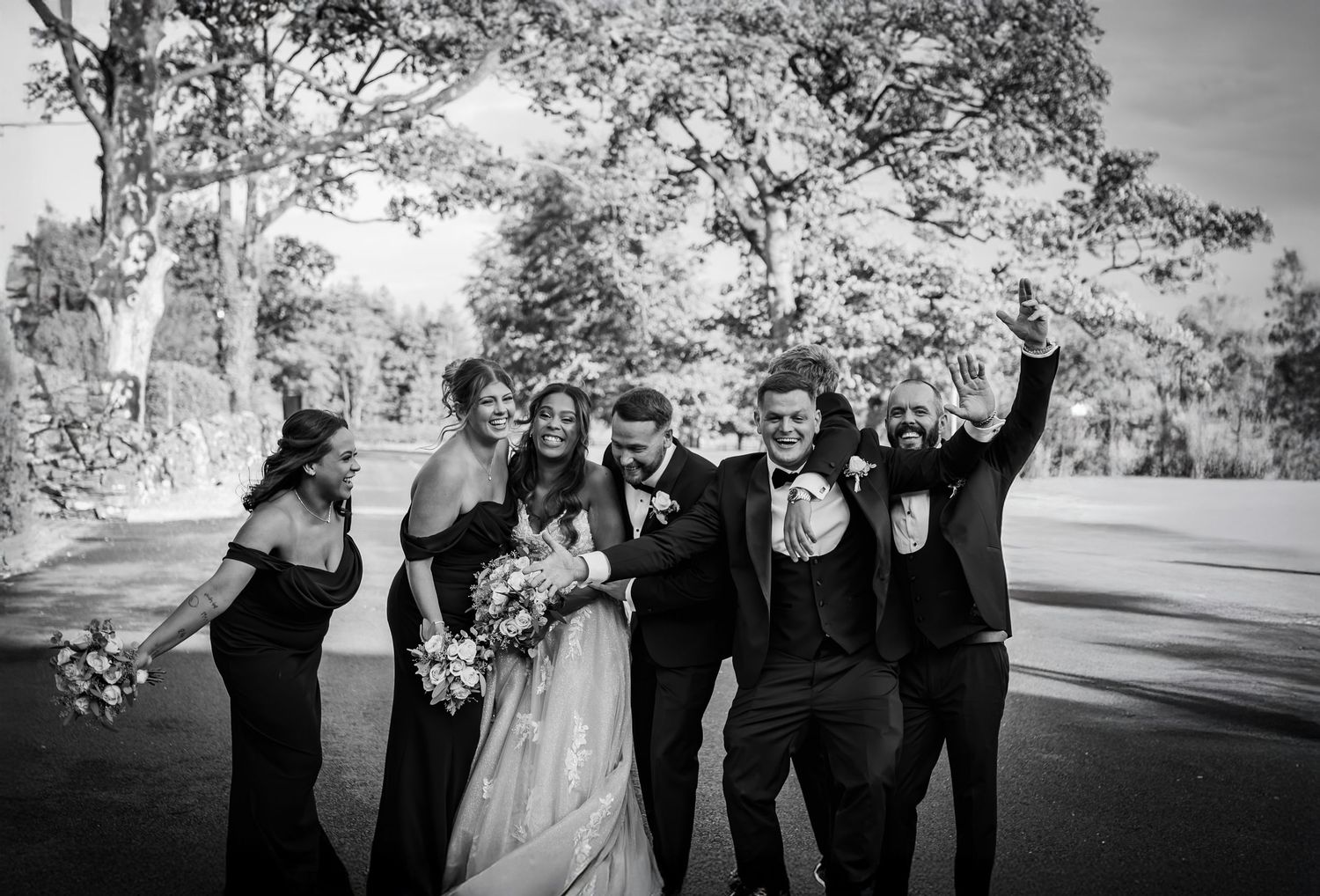 Wedding party in black attire walking and celebrating together on a tree-lined path during autumn.