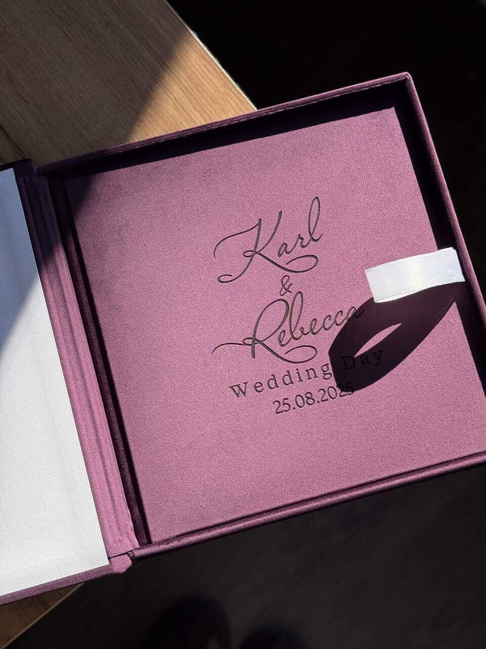 A pink wedding invitation book with cursive text and a date shows 25.08.23 in an elegant presentation box.