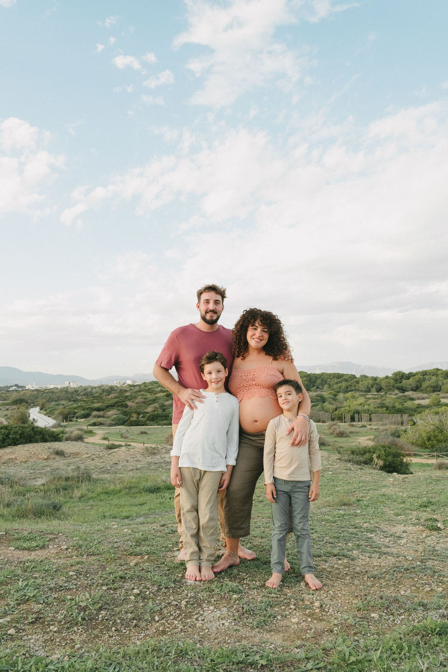 familia posando sobre un campo verde con un cielo azul durante su sesión de fotos de embarazo