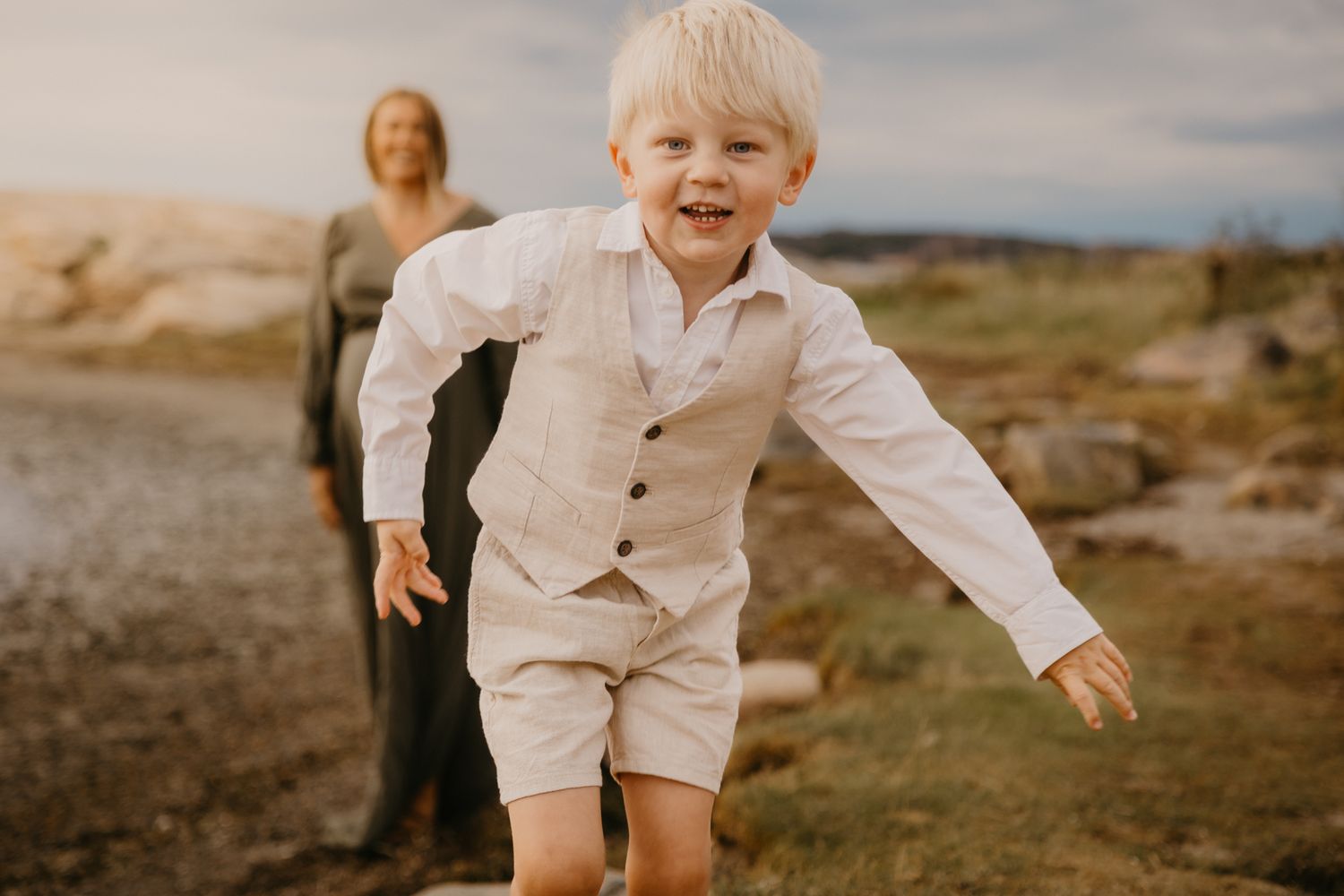 A child wearing a white shirt and shorts plays joyfully in a scenic outdoor setting at golden hour.
