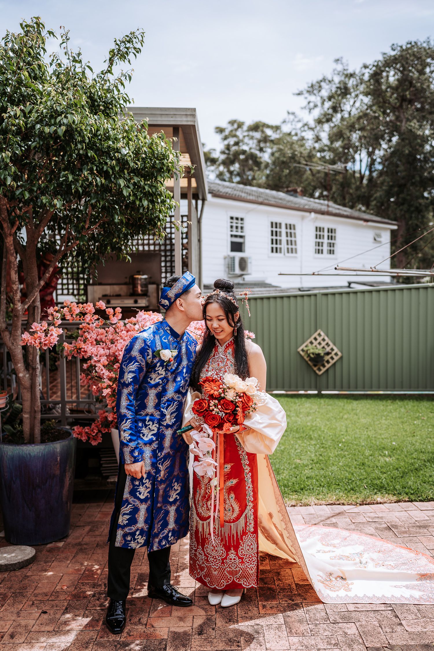 Traditional Chinese wedding couple in blue and red attire share a joyful moment together in a garden setting.