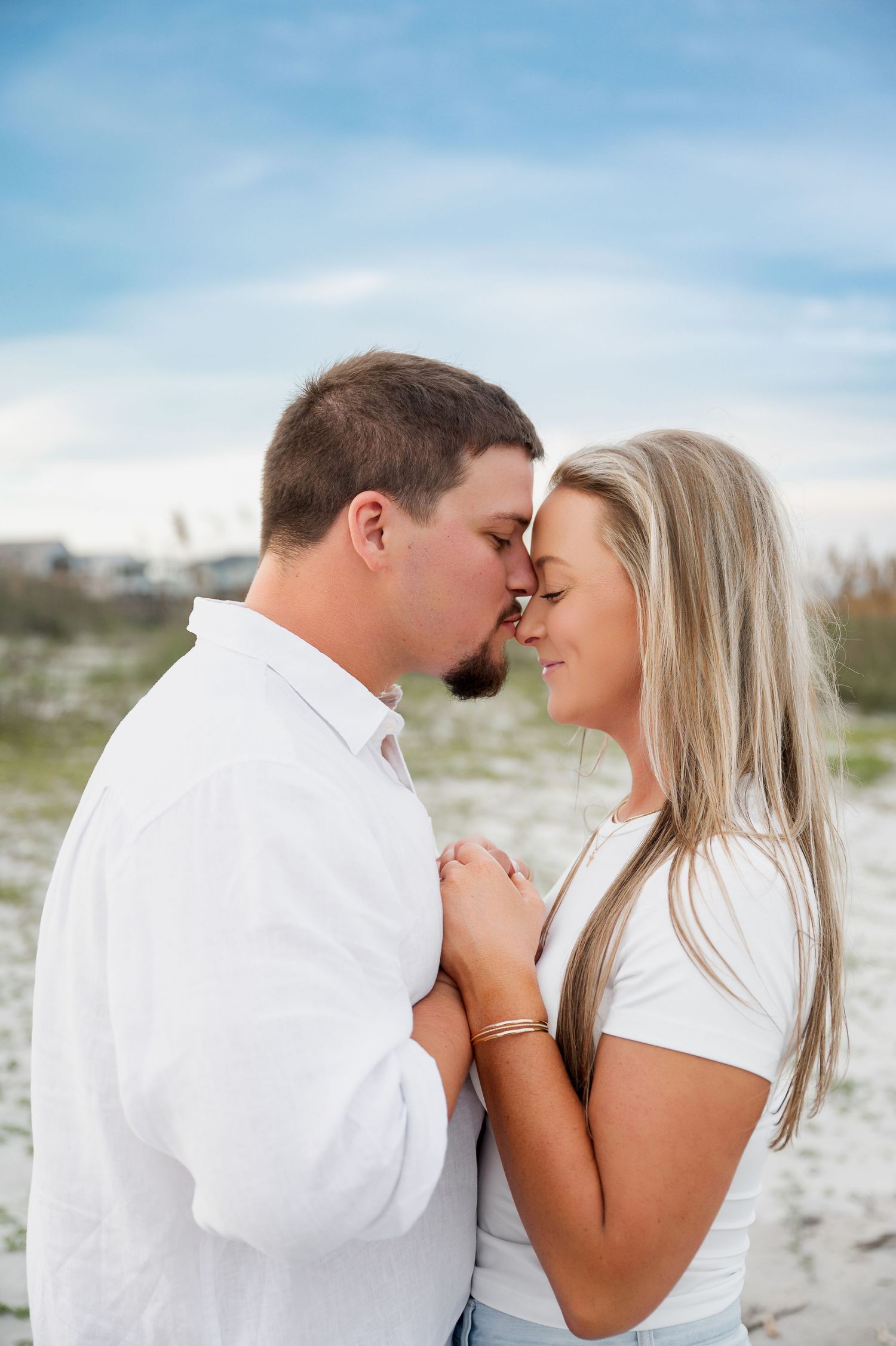 A couple in white clothing shares an intimate moment on a sandy beach.