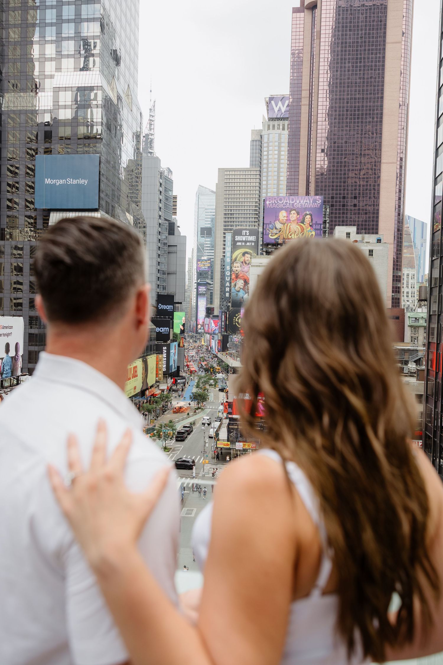 Wedding party waves from an urban balcony overlooking the city skyline with skyscrapers in the background.