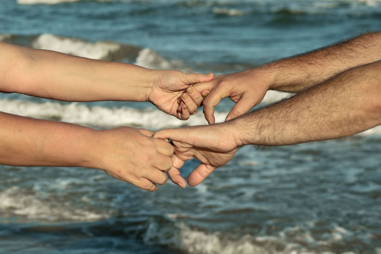 Seven connected images show hands reaching and holding each other against a blurred ocean background with waves.