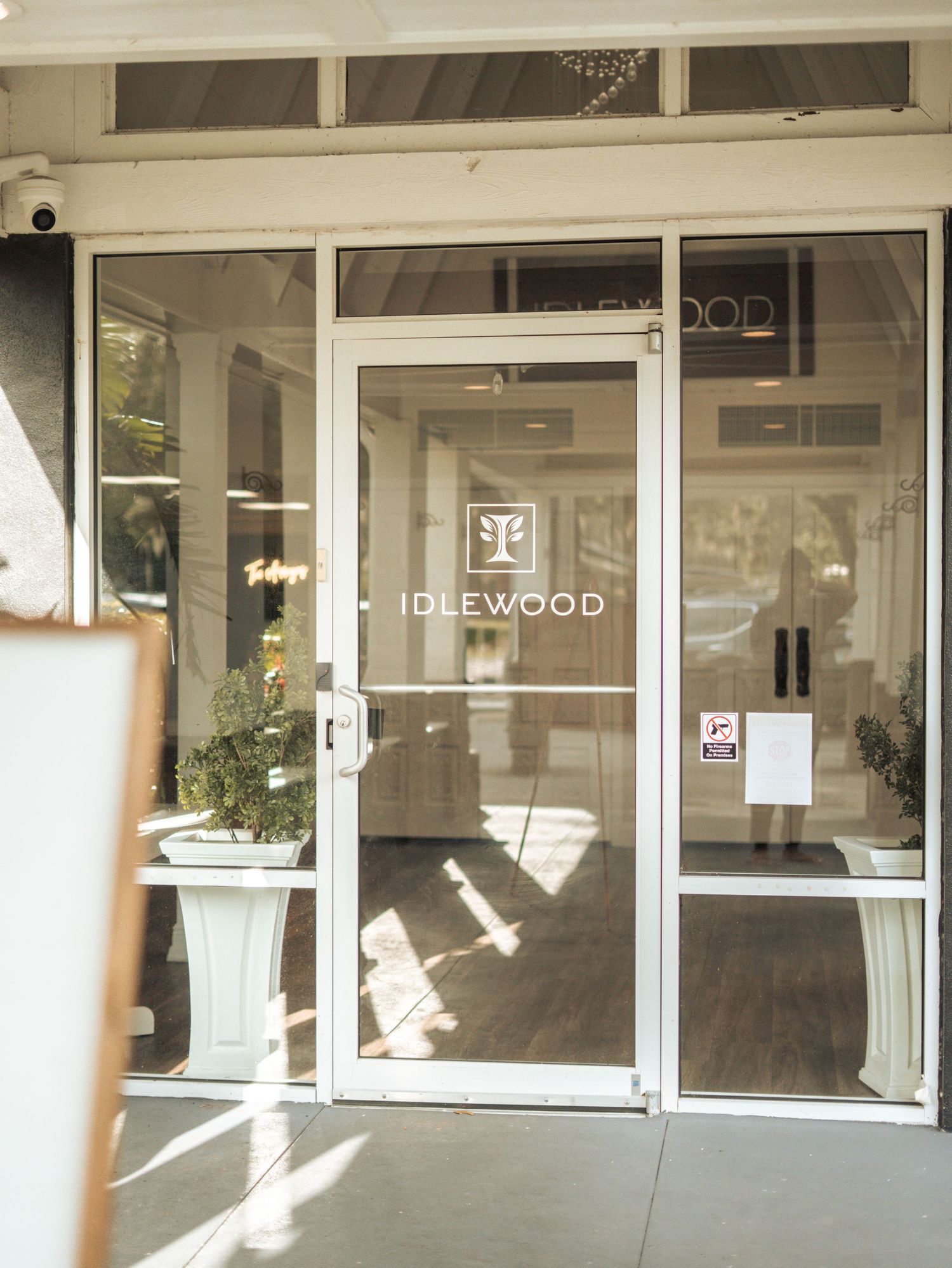 Glass storefront entrance of Idlewood building with white lettering and sunlight streaming through the glass door.