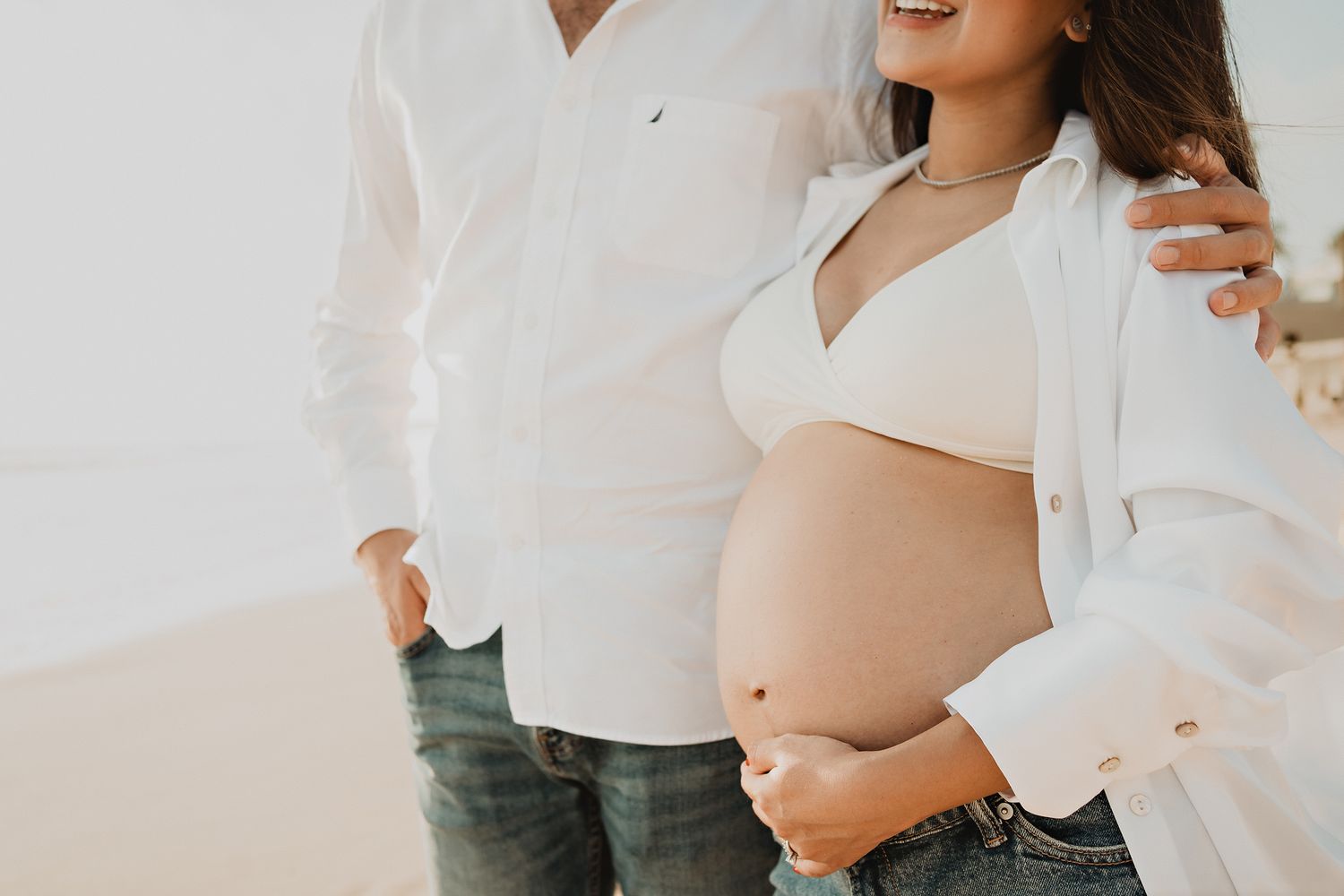 Couple embracing, the wife showcasing her baby bump with a bright smile, capturing the beauty of pregnancy in Mazatlán