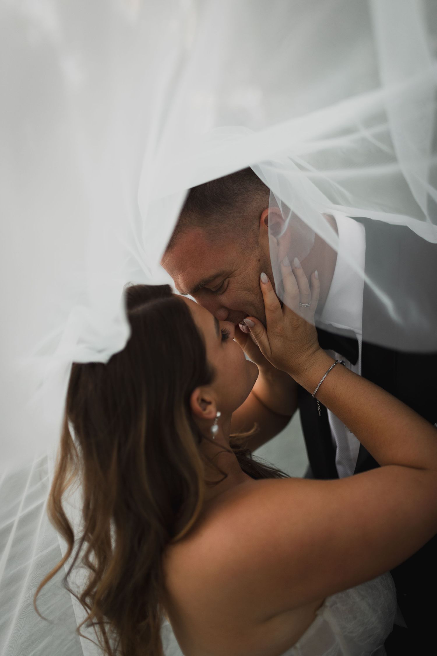 A romantic wedding moment captured under flowing white veil as couple shares an intimate kiss.
