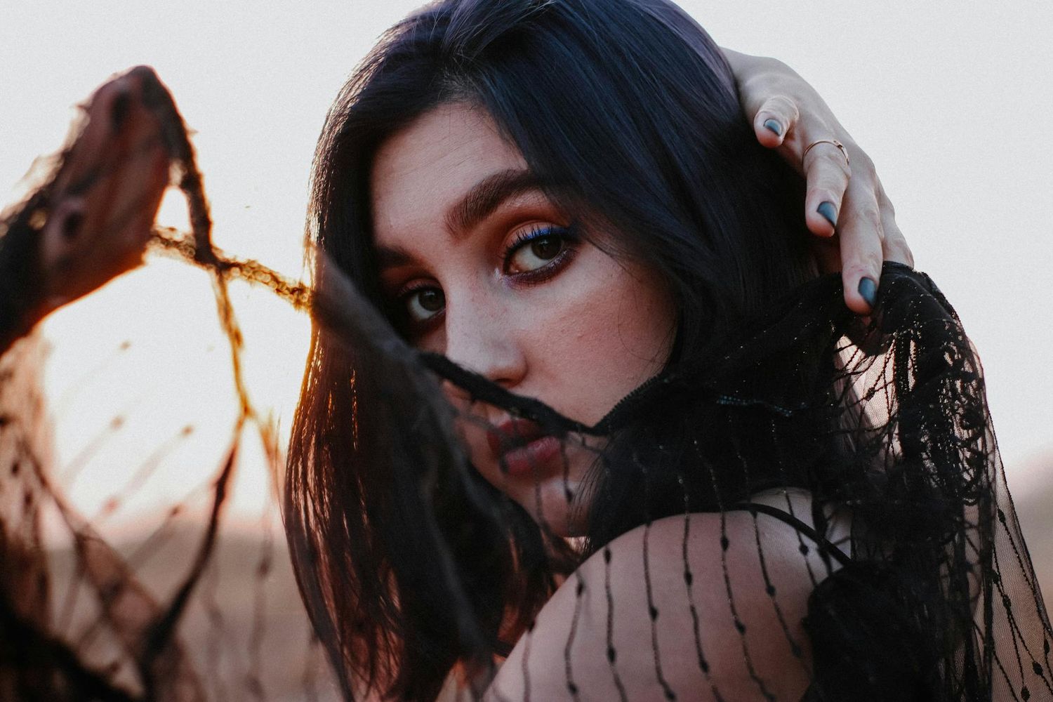 A dark-haired person in black lace poses dramatically against a sunset sky in an artistic portrait. Pittsburgh Boudoir