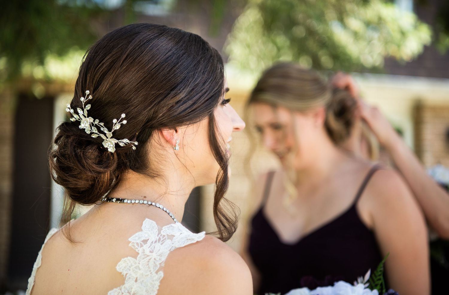 Delicate floral hairpiece adorns an elegant updo hairstyle with lace dress detail visible from behind.