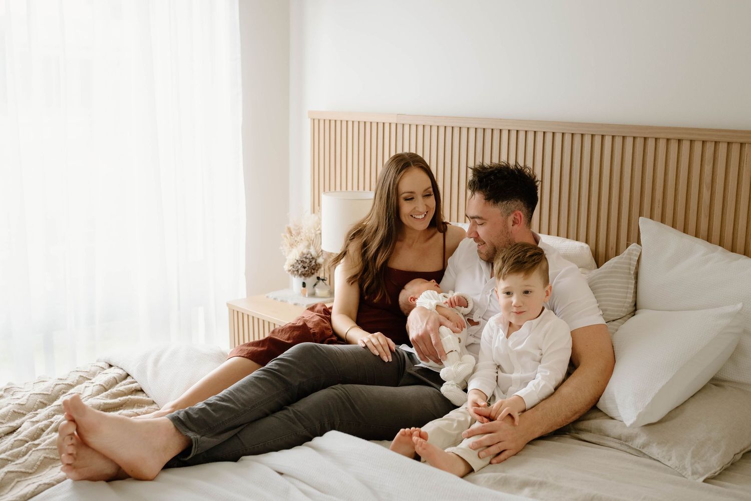 Young family relaxing together on bed with baby in bright modern bedroom.