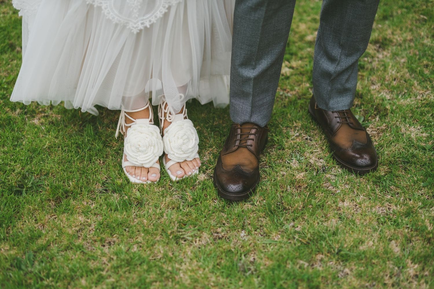 Feet and shoes of a bridal couple standing together on green grass in a wedding photo.