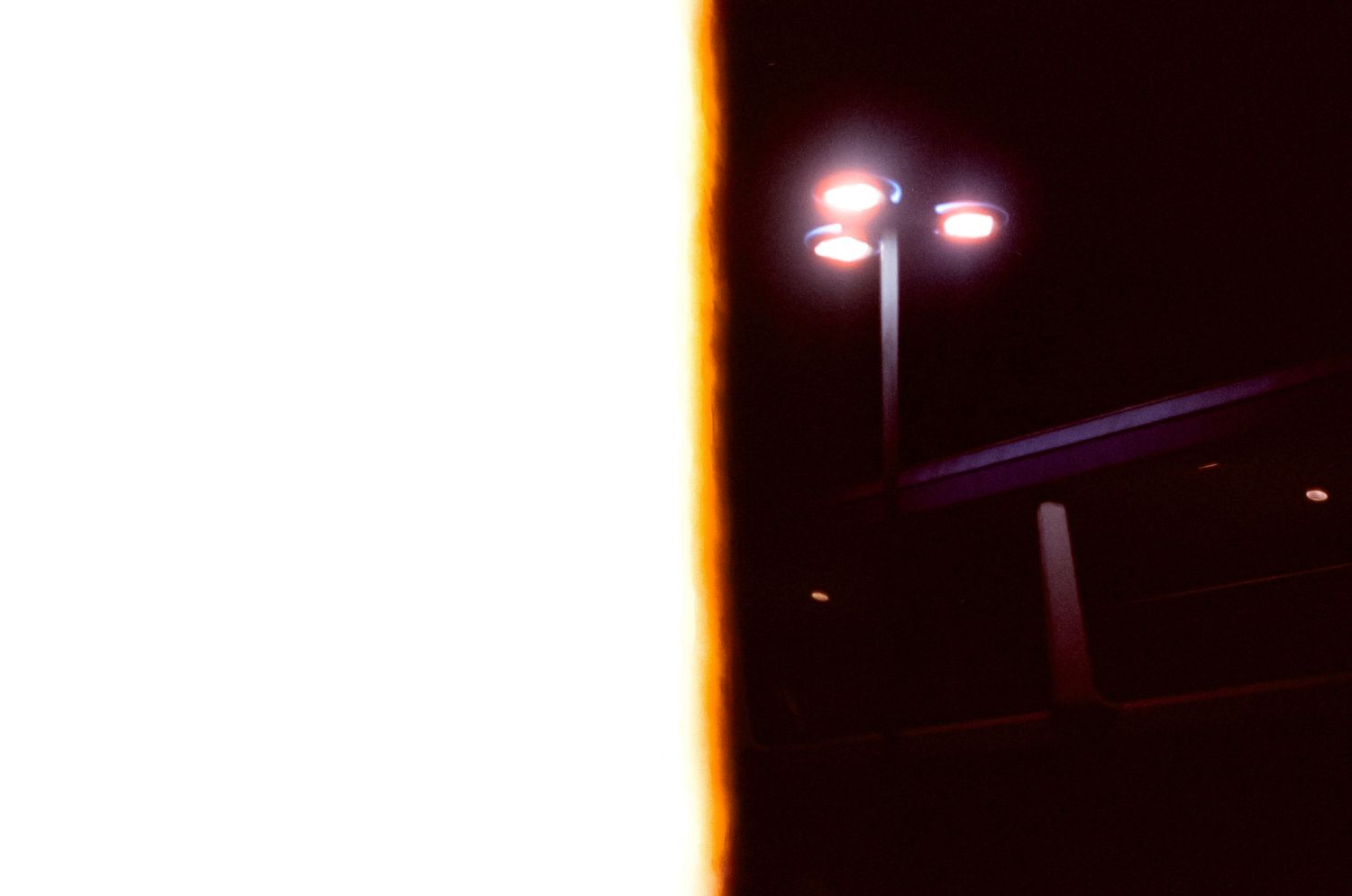 Street lamp glowing in dark night sky with bright orange light leak.