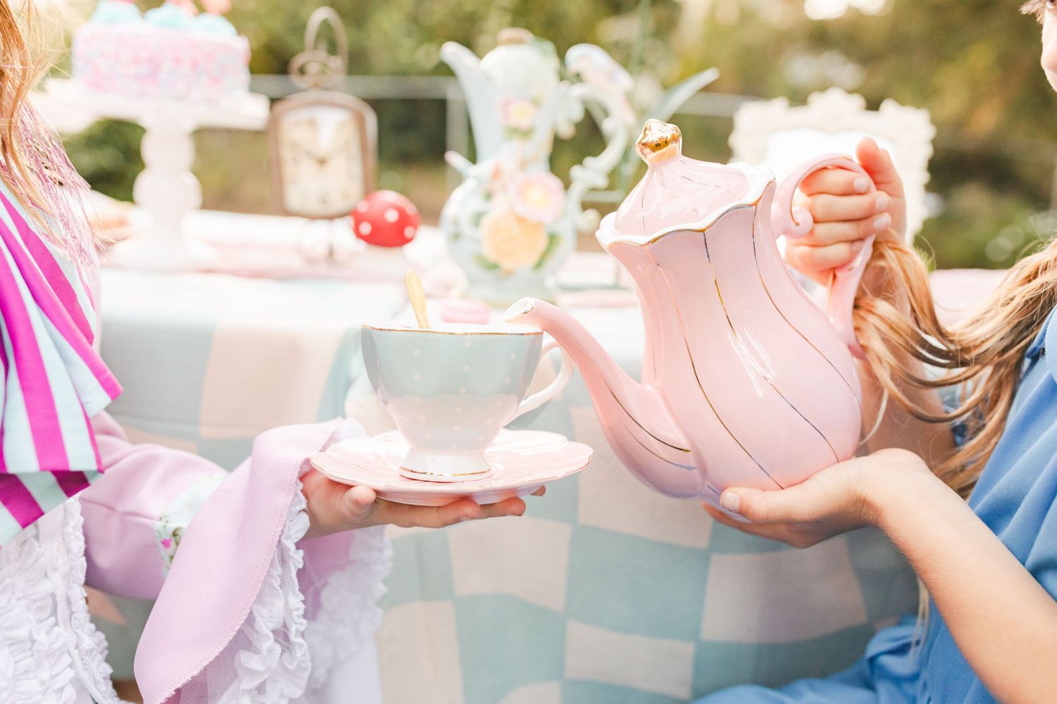 Whimsical tea party scene with pink teapot and vintage teacups on checkered tablecloth.Film by Chelsee Rawe Photography