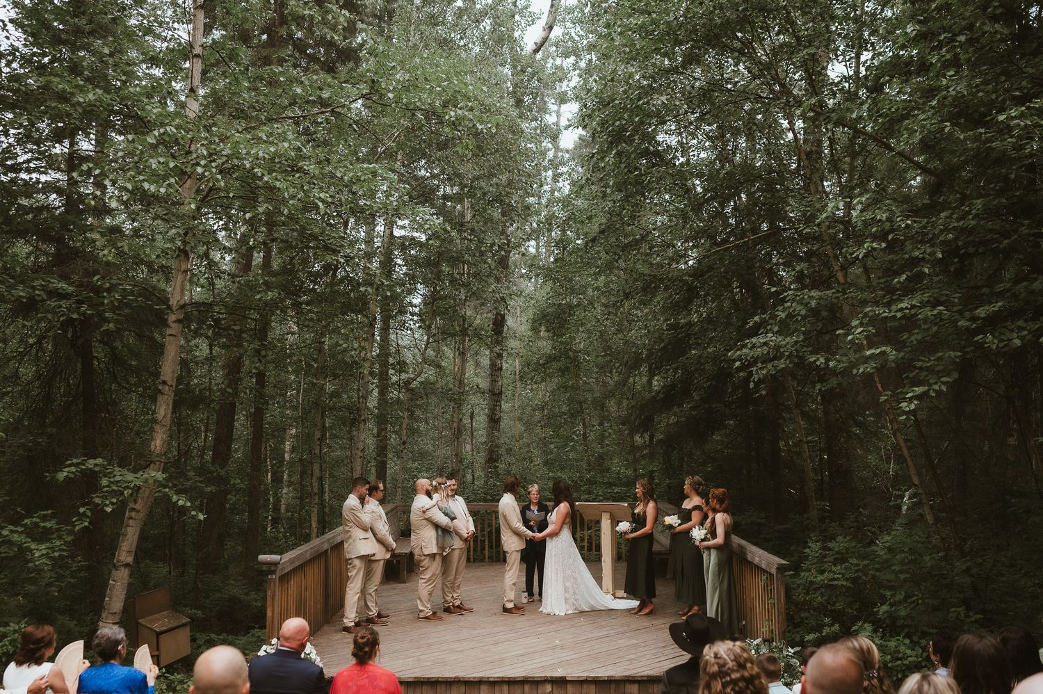 Forest wedding ceremony on a wooden platform surrounded by tall evergreen trees.
