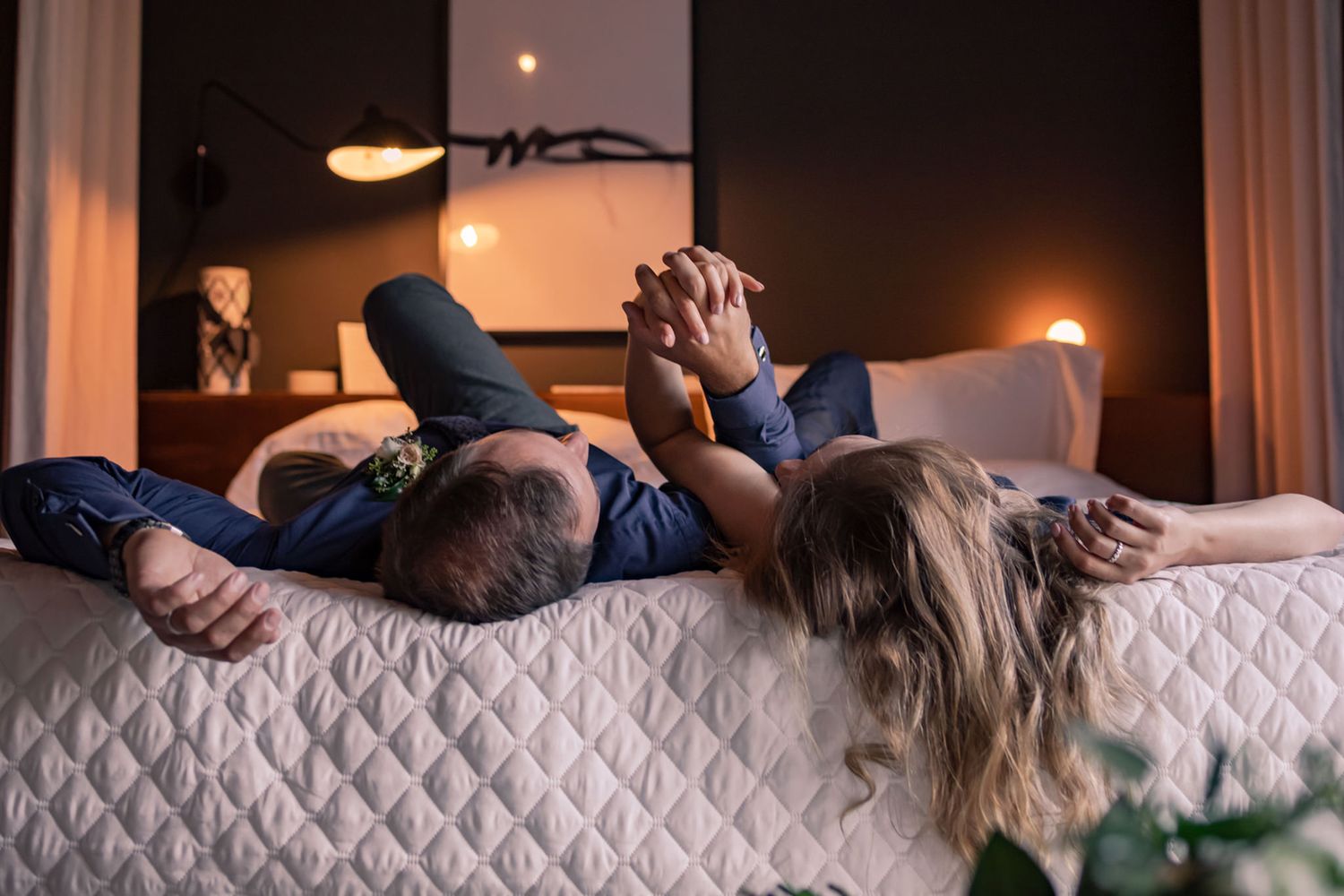 Couple holding hands on bed during anniversary shoot at Rosemont Inn, Kingston, Ontario, captured by Lumenali Photography.