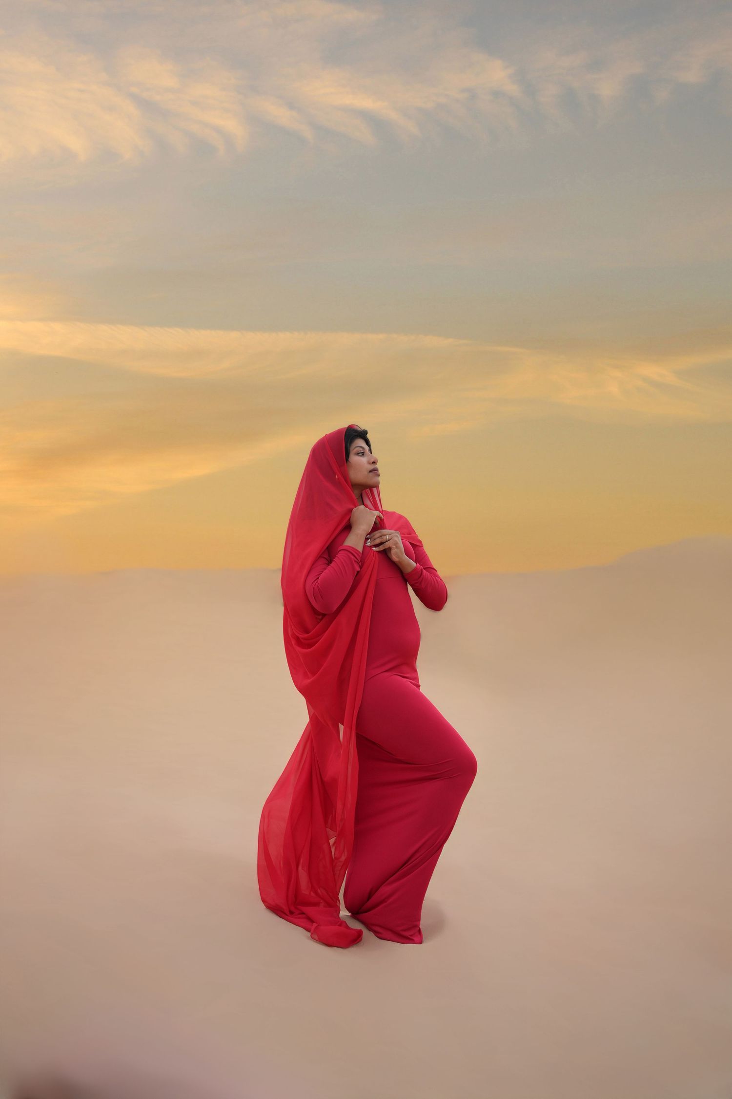 A figure in flowing red fabric poses elegantly against a misty golden sunset sky.