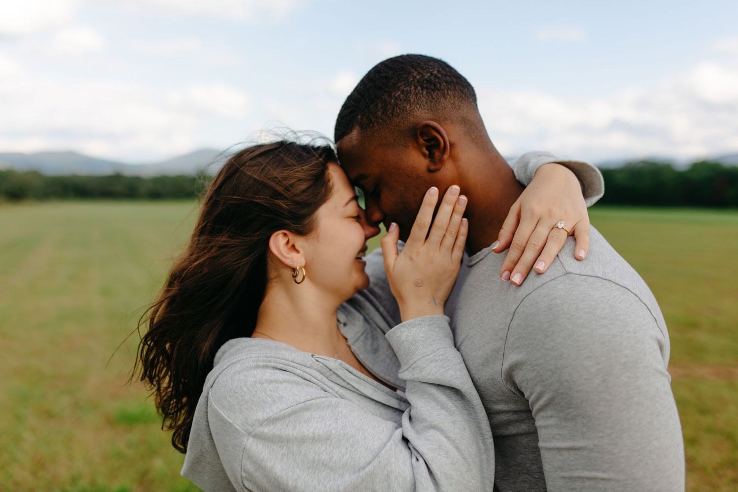 Intimate couple embracing in sunny field with mountains in background.