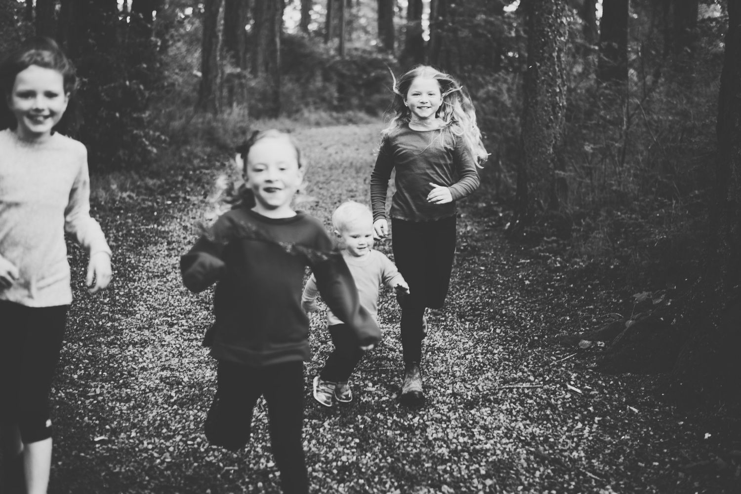 Three children running joyfully along a forest path, captured in black-and-white for an authentic, playful family moment