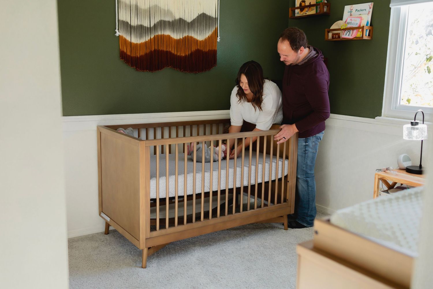 A mom and dad stood over a crib, mom leaning into the crib, her hands placed on the head of a newborn girl.  Man snuggled close to the mom.