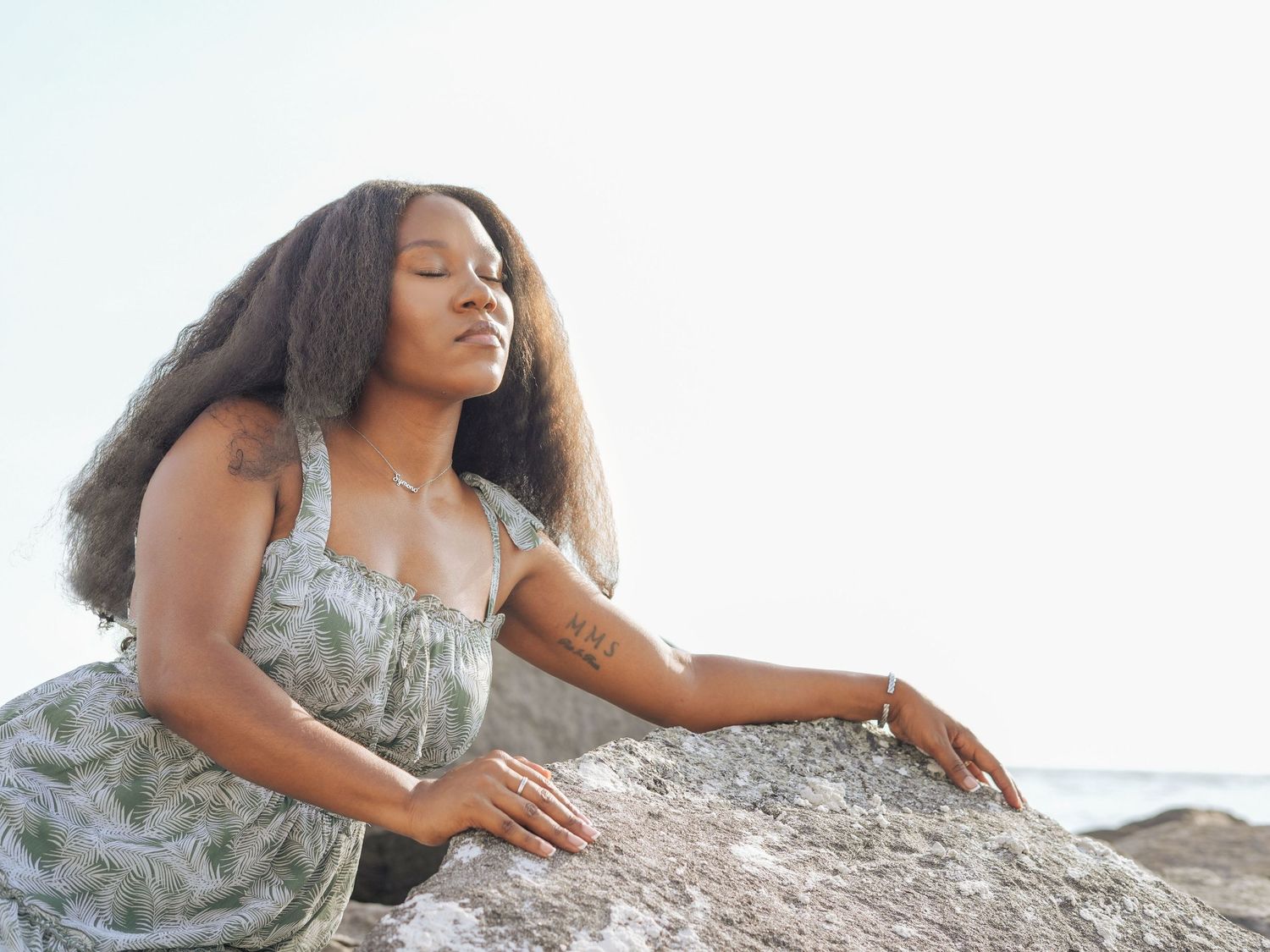 A person in a patterned dress reclines on coastal rocks during a photoshoot.