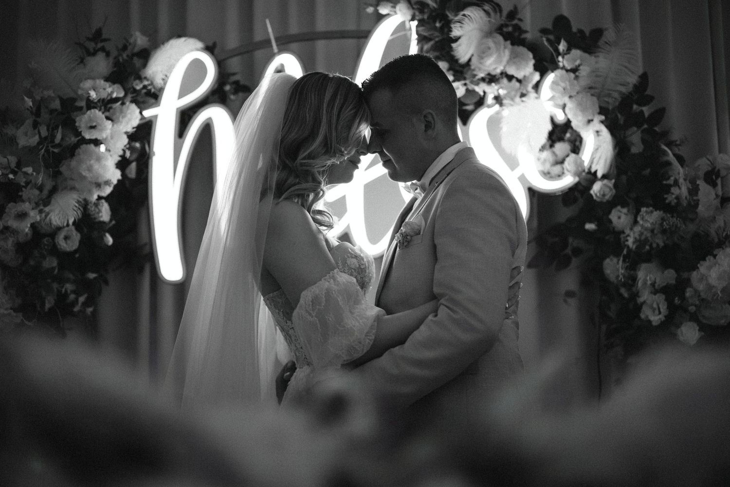 A romantic black and white moment between newlyweds in front of an illuminated neon sign.