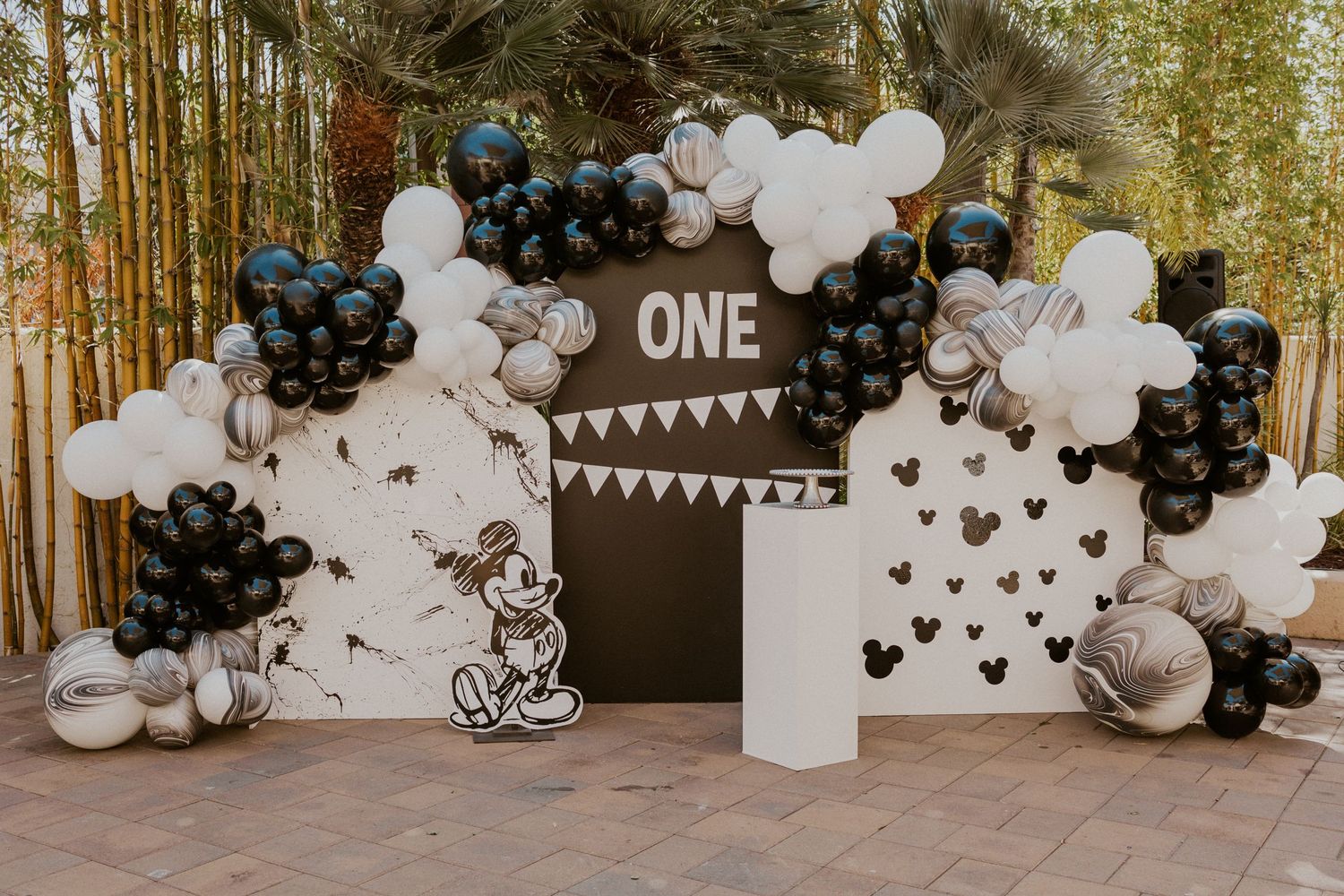 Mickey Mouse themed first birthday party decoration with black and white balloon arch and backdrop.