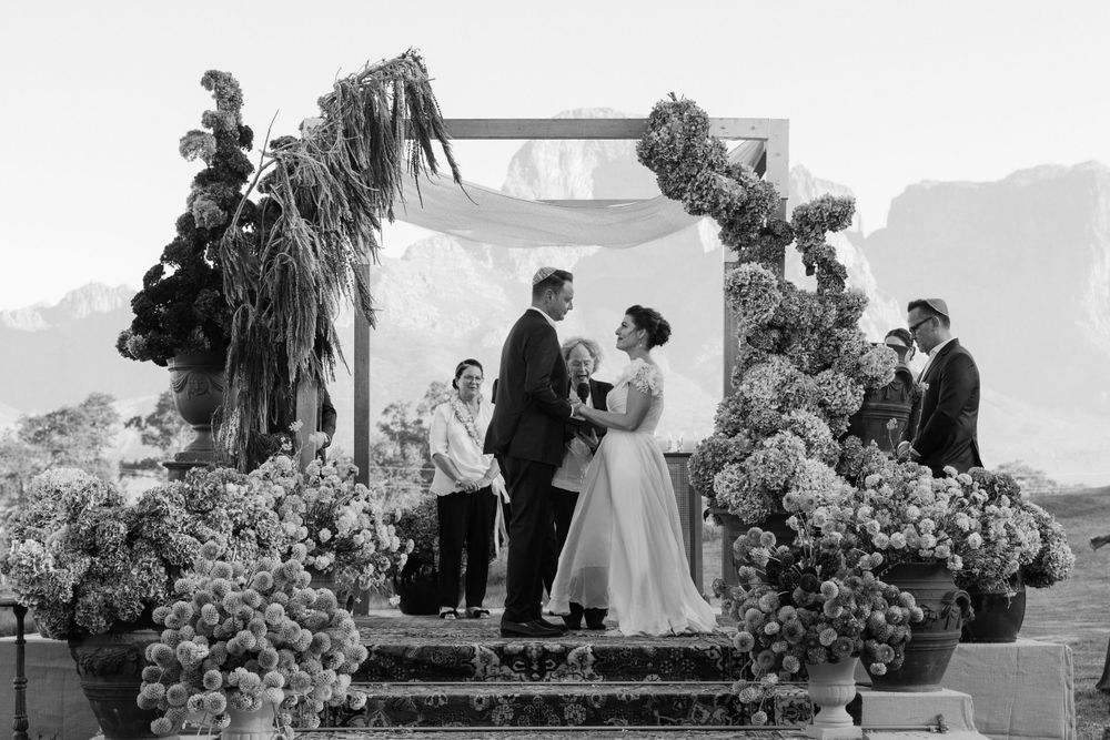 wedding ceremony under floral arch with mountains in background.