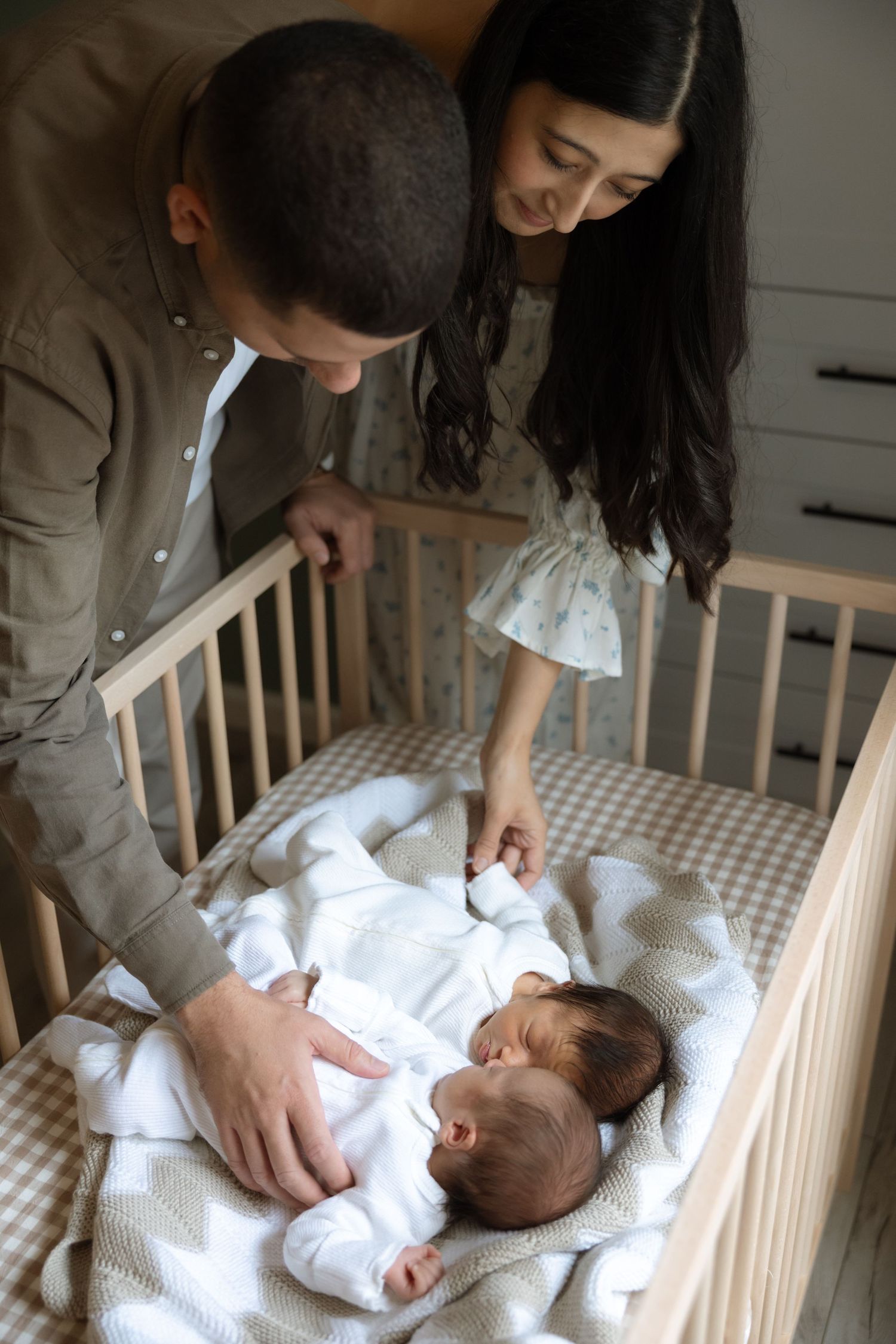 Parents lovingly gazing at their newborn baby lying in a wooden crib with a checkered blanket.