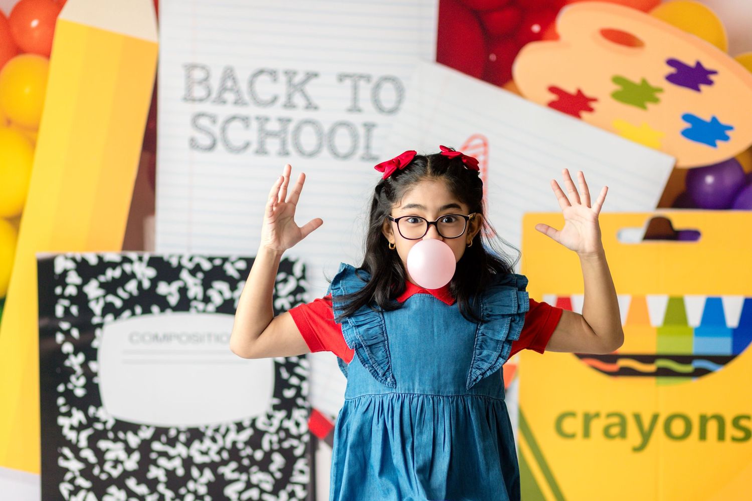 Child smiling and holding a backpack in a colorful back-to-school mini photoshoot setup, with school-themed props