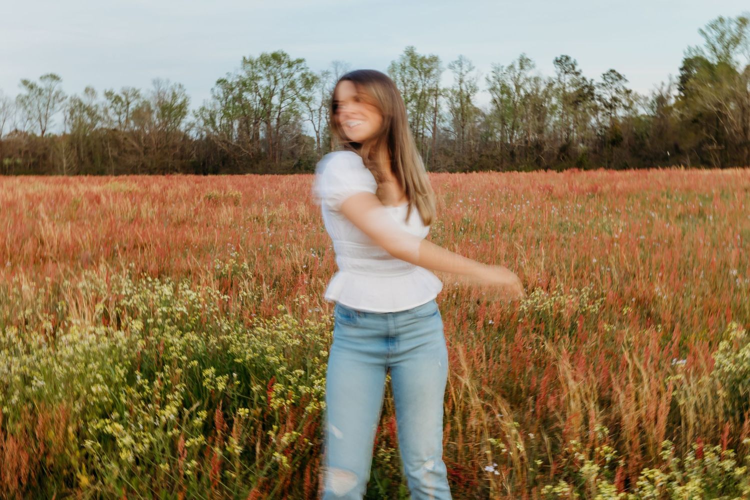 Figure in a white t-shirt and jeans stands in a vibrant field of red wildflowers during golden hour.
