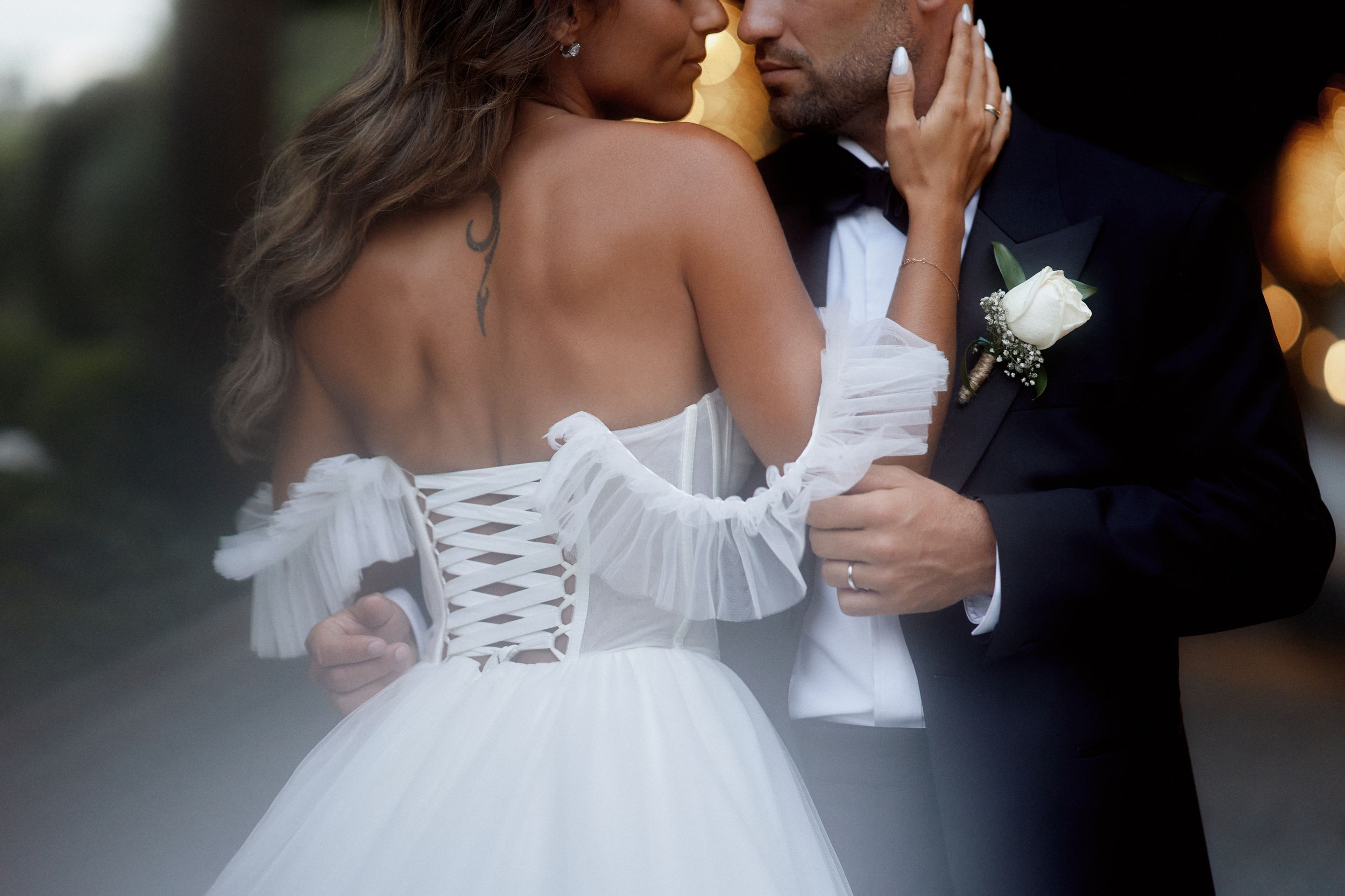 Close-up detail of a bride in a white corset dress embracing during a romantic wedding moment.
