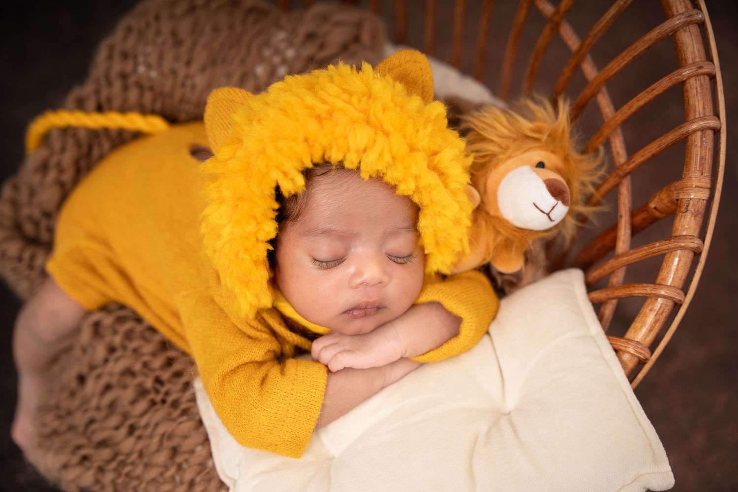 Sleeping baby wearing yellow lion costume in wicker basket with knit blanket.