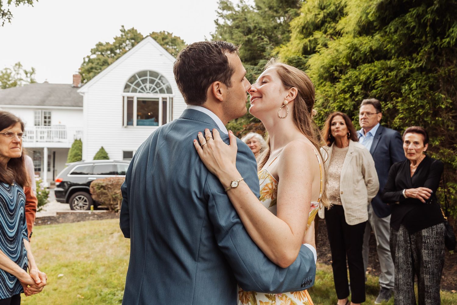 A couple shares their first kiss during an outdoor wedding ceremony while guests look on.