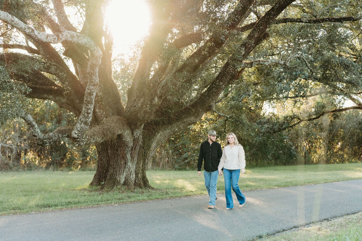 A couple takes a relaxing sunset stroll under a large oak tree on a peaceful pathway.