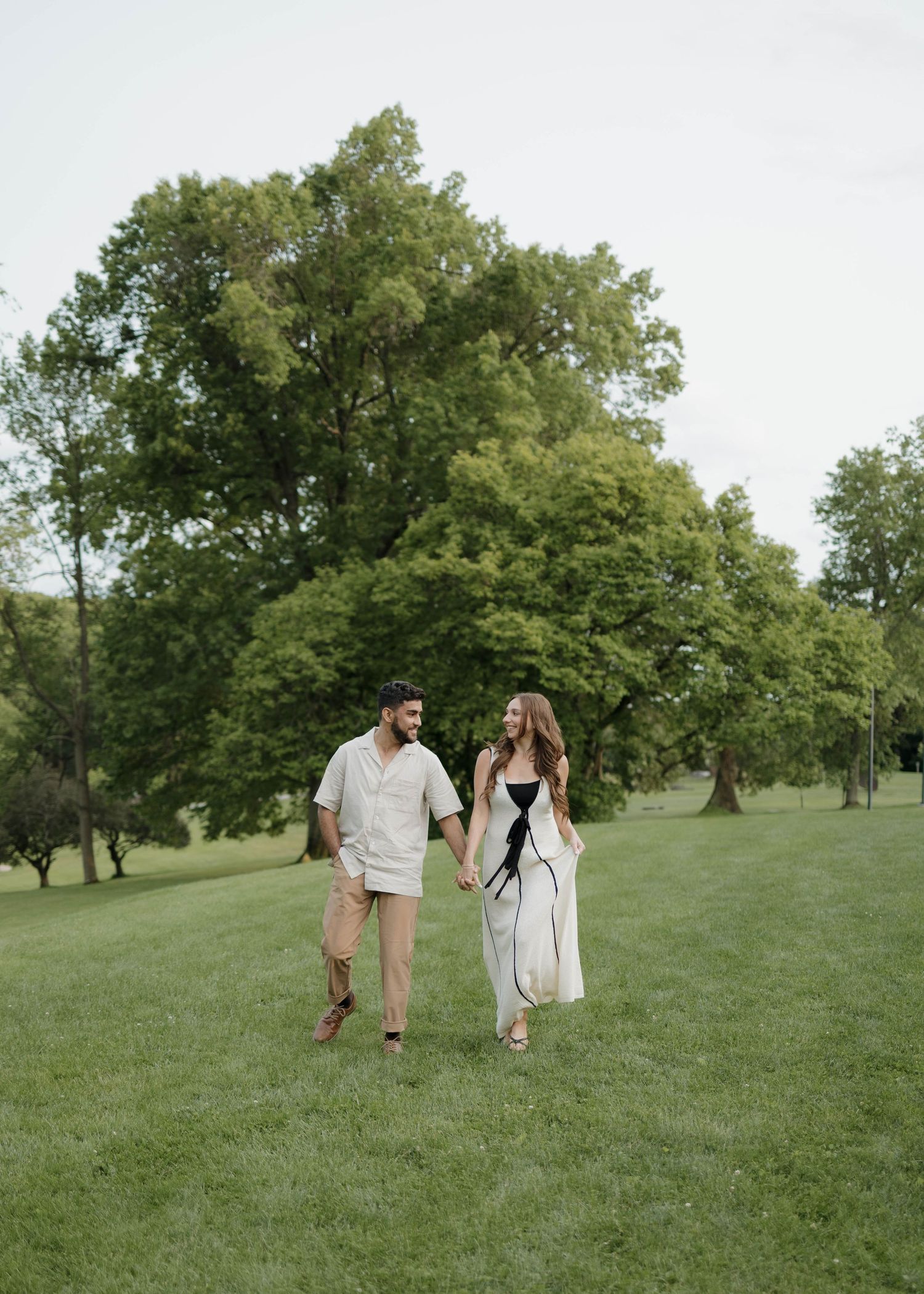 Romantic marriage proposal scene on a grassy lawn near a stone building as onlookers watch in the background.