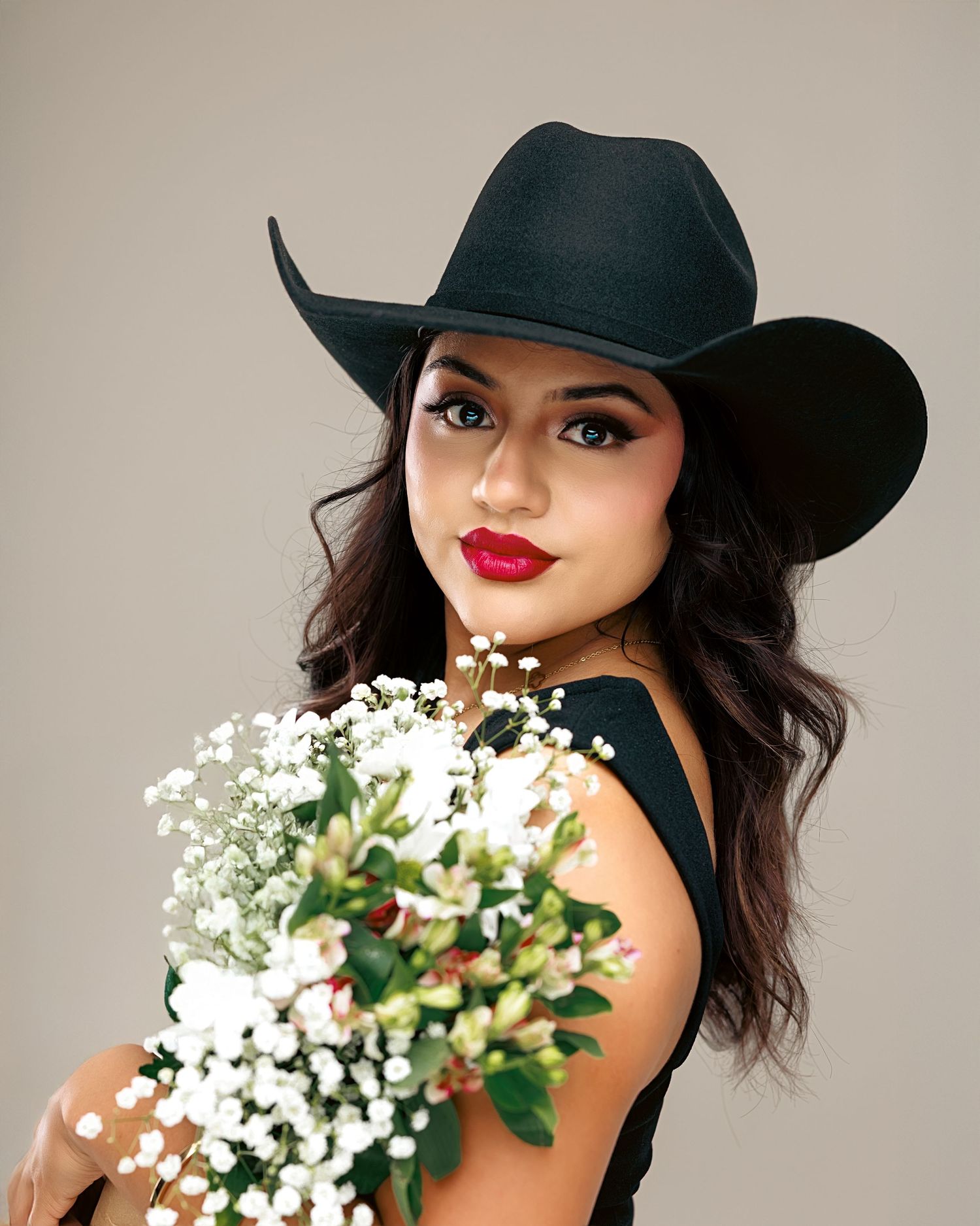 Stylish portrait of someone in a black hat with red lipstick and white flowers against a neutral background.