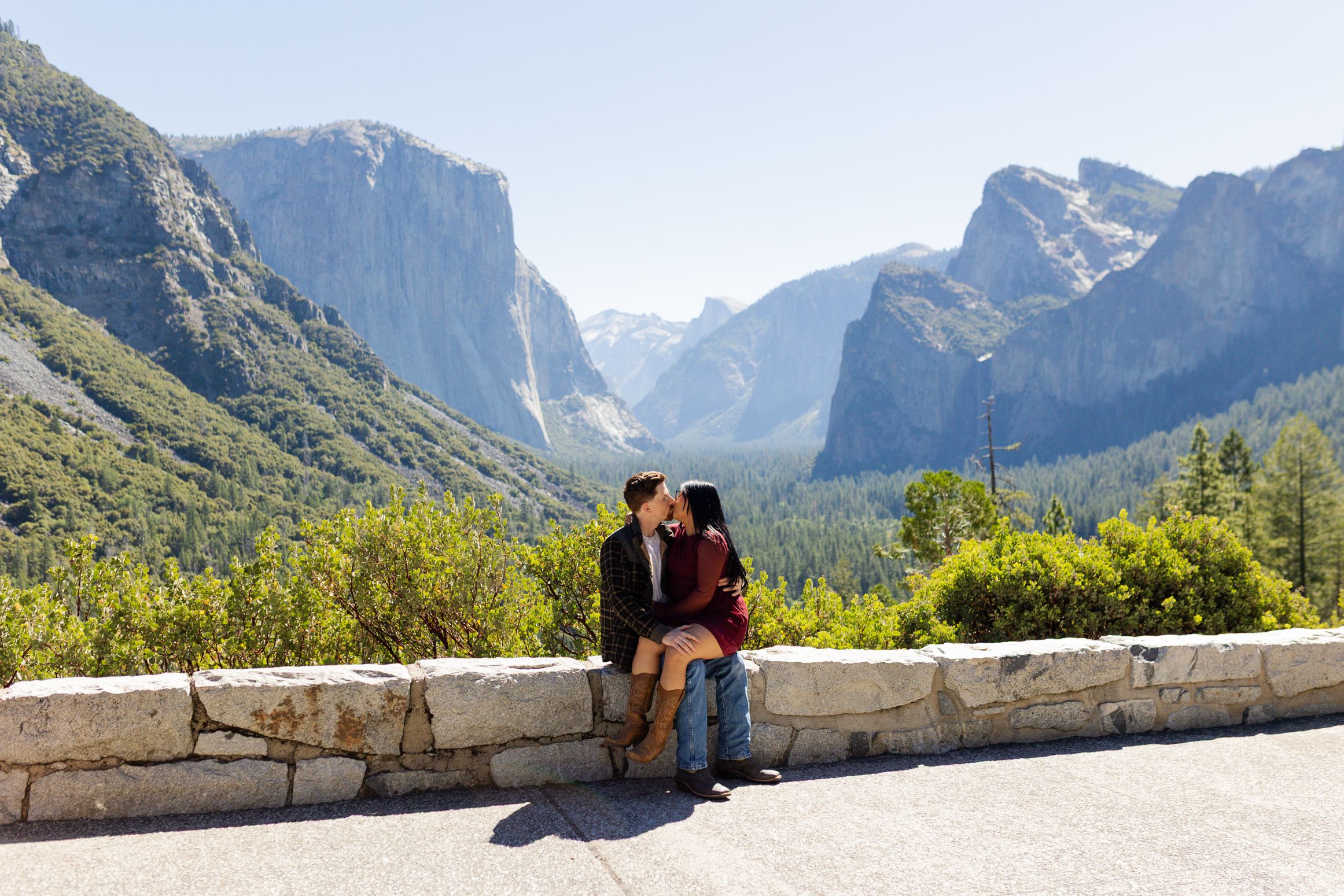 Couple kissing at Yosemite Valley tunnel view overlook with El Capitan and waterfalls in background.