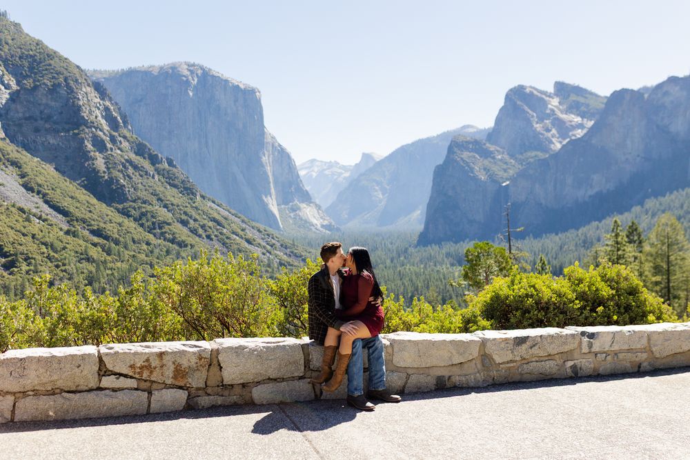Couple kissing at Yosemite Valley tunnel view overlook with El Capitan and waterfalls in background.