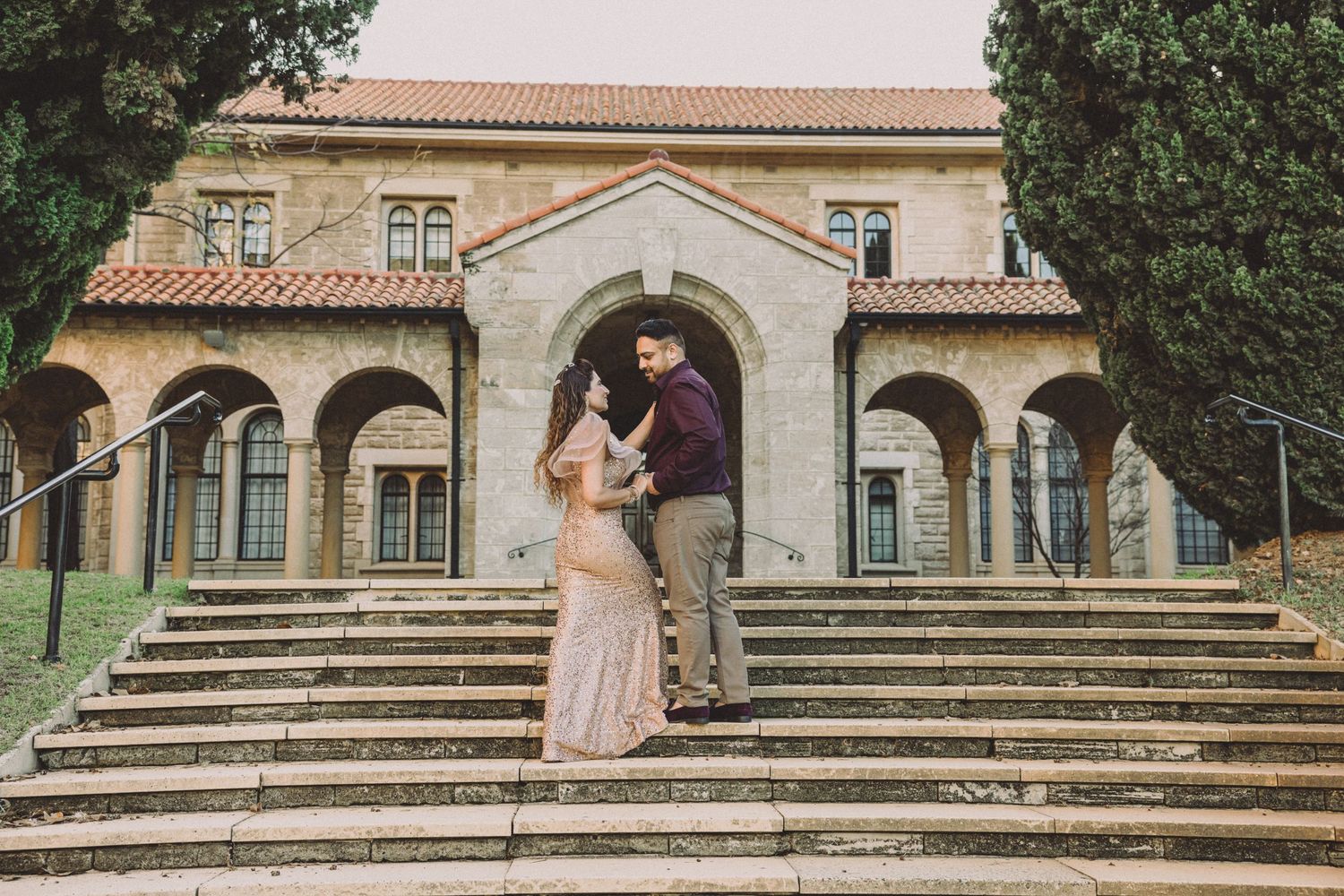Couple sharing a romantic moment on stone steps of a historic building with arched colonnades.
