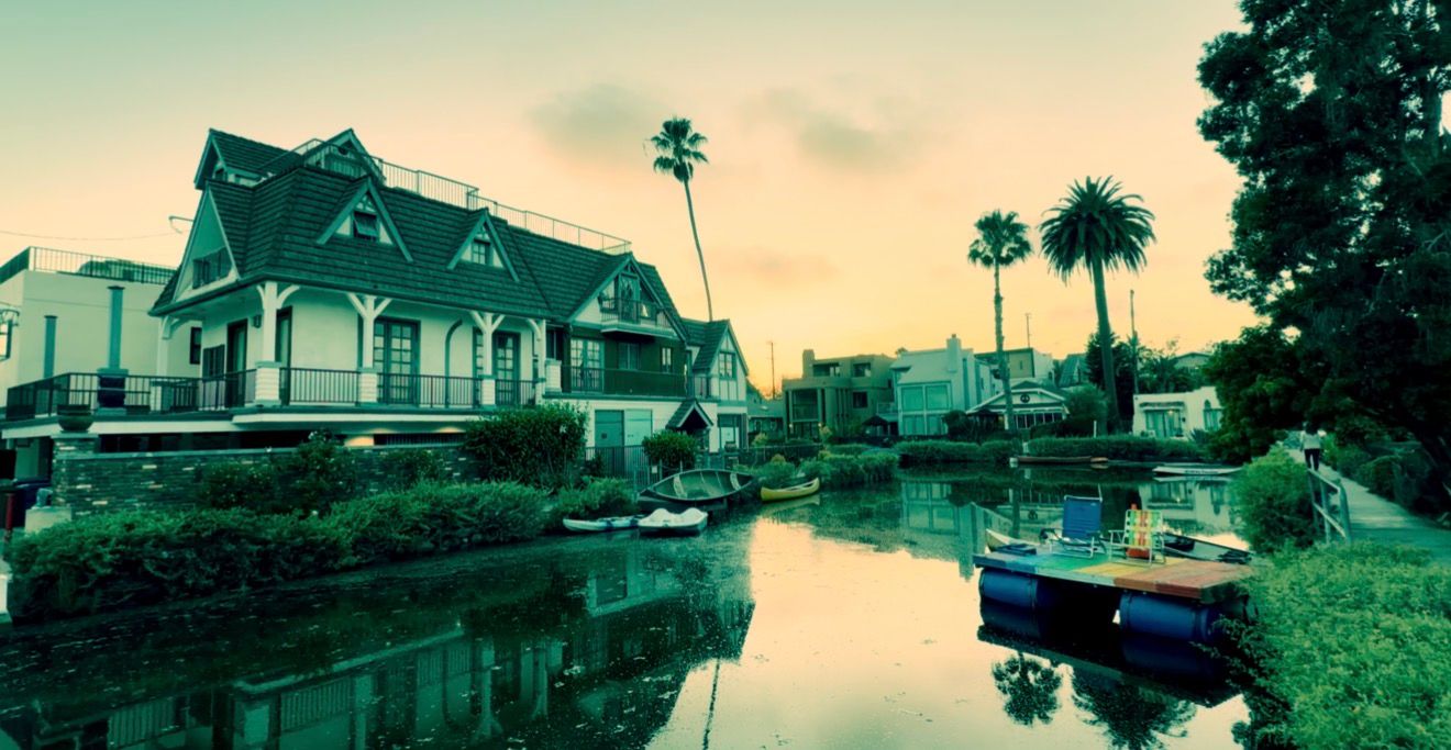 Scenic Venice Canal at sunset with colorful boats, lush palm trees, and charming waterfront homes reflecting in calm water.