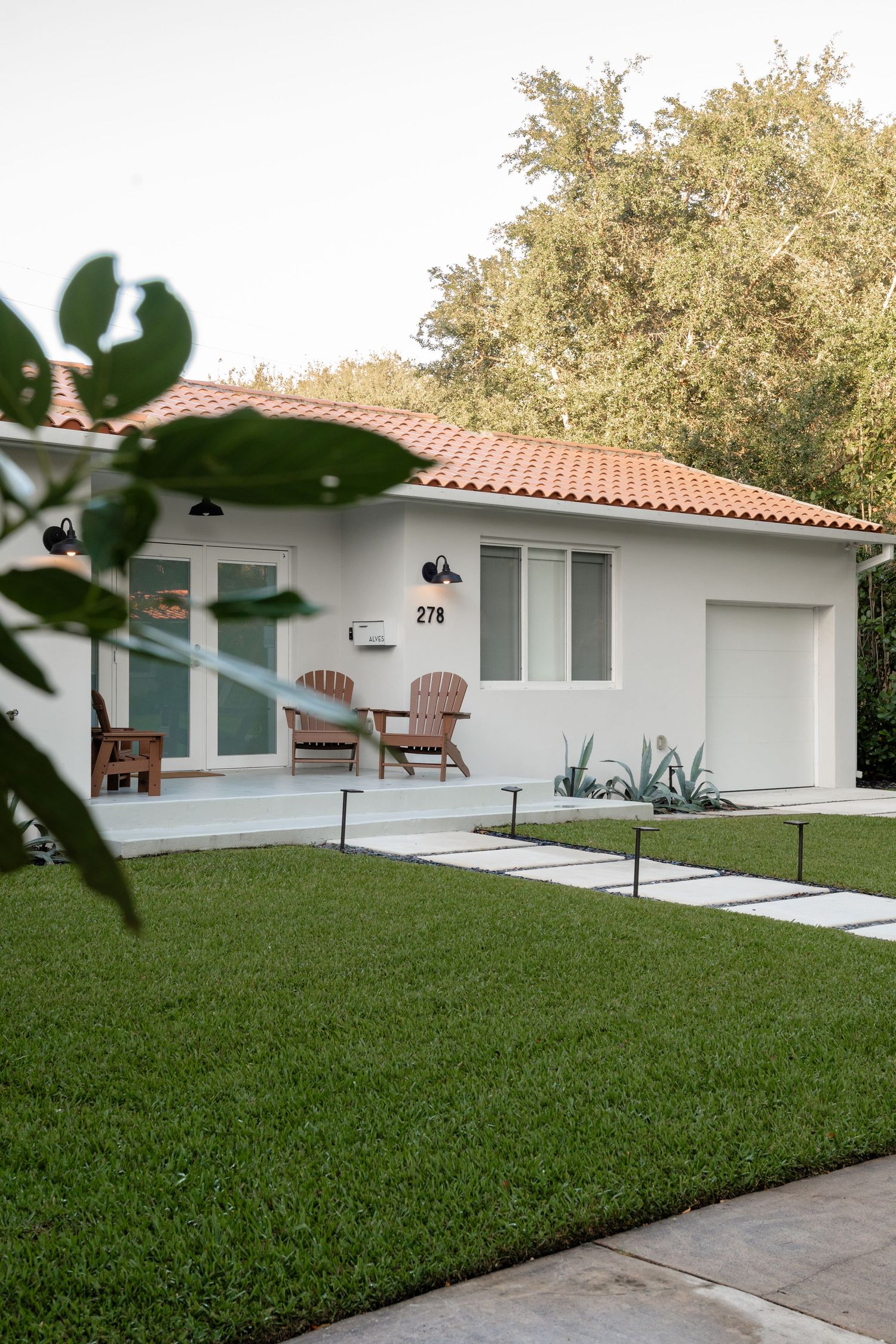 White stucco home with red tile roof, Adirondack chairs on porch, manicured lawn, and stepping stone path at 278.
