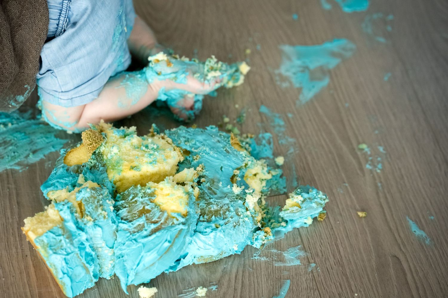 Baby smashing blue frosted birthday cake on floor during first birthday cake smash photo session.