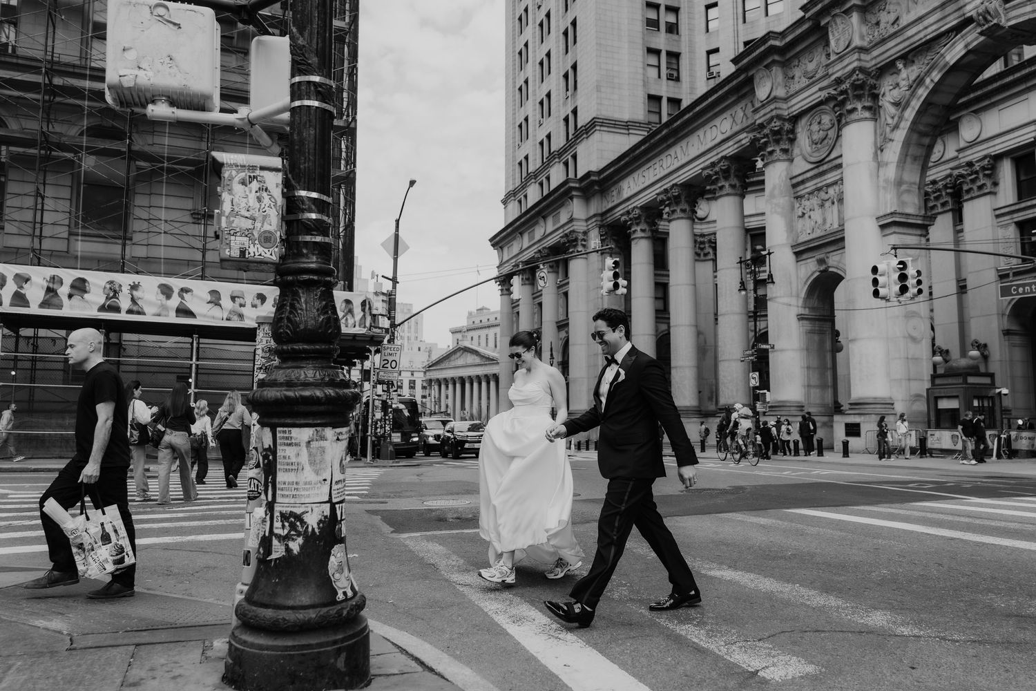 Black and white photo of a bride and groom crossing a busy city street, with grand buildings in the background.
