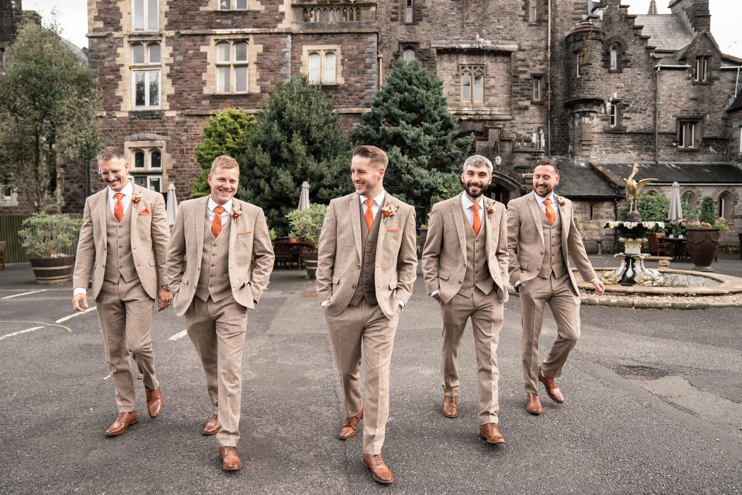 A wedding couple poses in coordinated outfits featuring a grey tweed suit and white lace dress with autumn-themed bouquet.