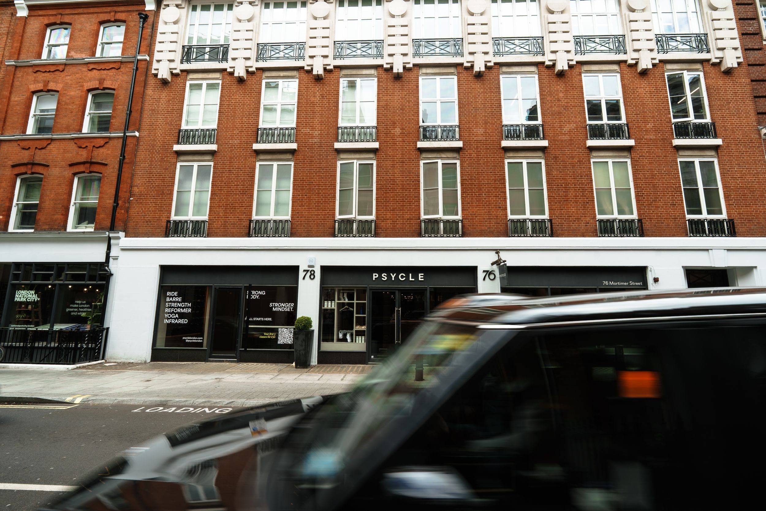Psycle fitness studio exterior on a London street with a red double-decker bus passing by the brown brick building.
