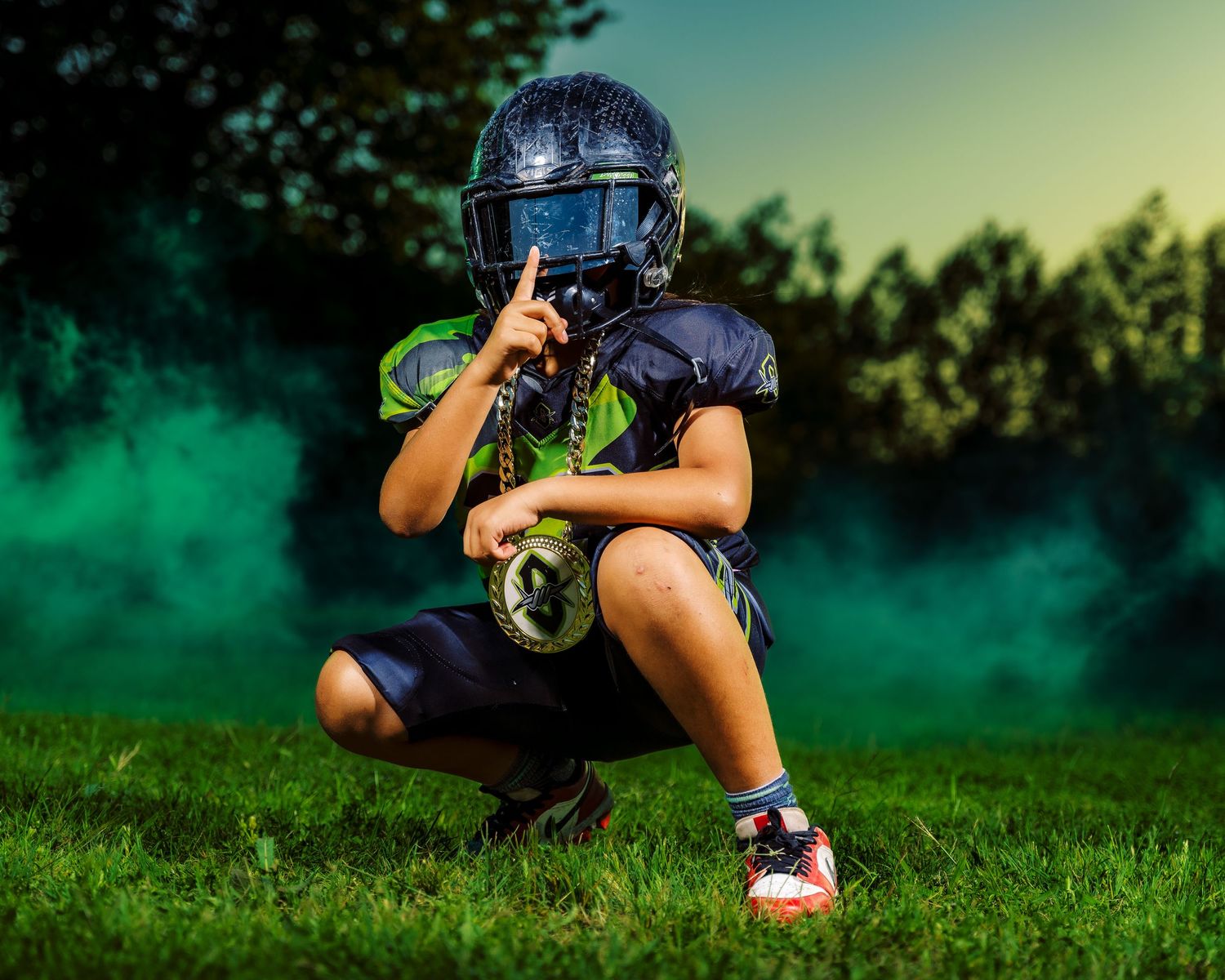 Young football player in navy uniform and helmet crouching on grass field with dramatic green smoke background.