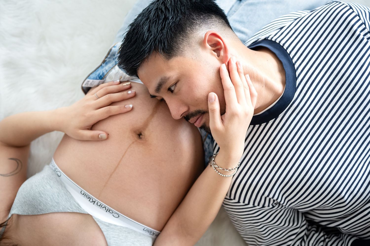 A person lying down appears to be experiencing a headache or migraine while resting on a bed.