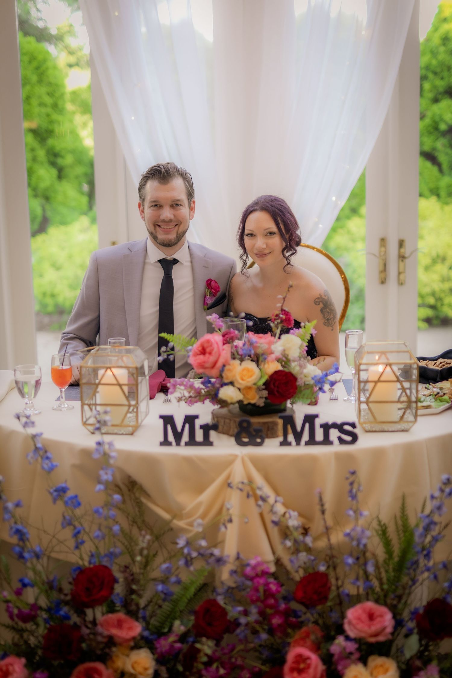 Wedding ceremony takes place under a rustic wooden pavilion with exposed beams and scenic view through archway in background.