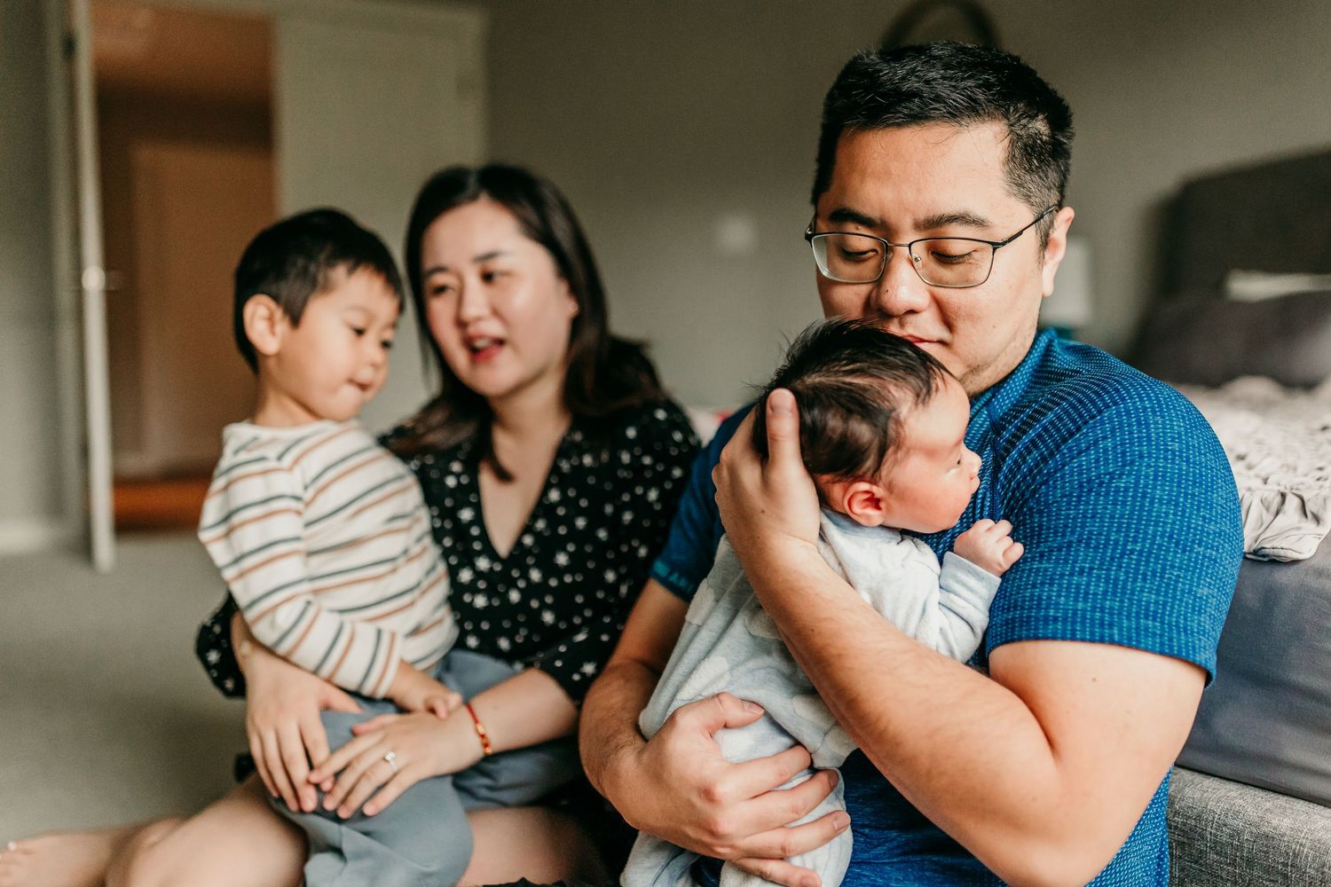 Asian family with toddler and newborn baby share a tender moment together at home.