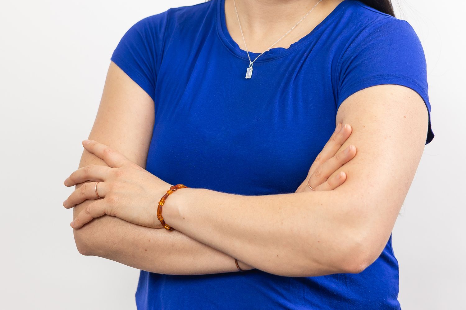 woman crossing arms in headshot, detail crop of just arms wearing amber bracelet and copper rings and blue short sleeve shirt in Tacoma, WA